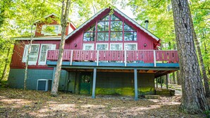 A two-story cabin with a balcony, surrounded by trees.