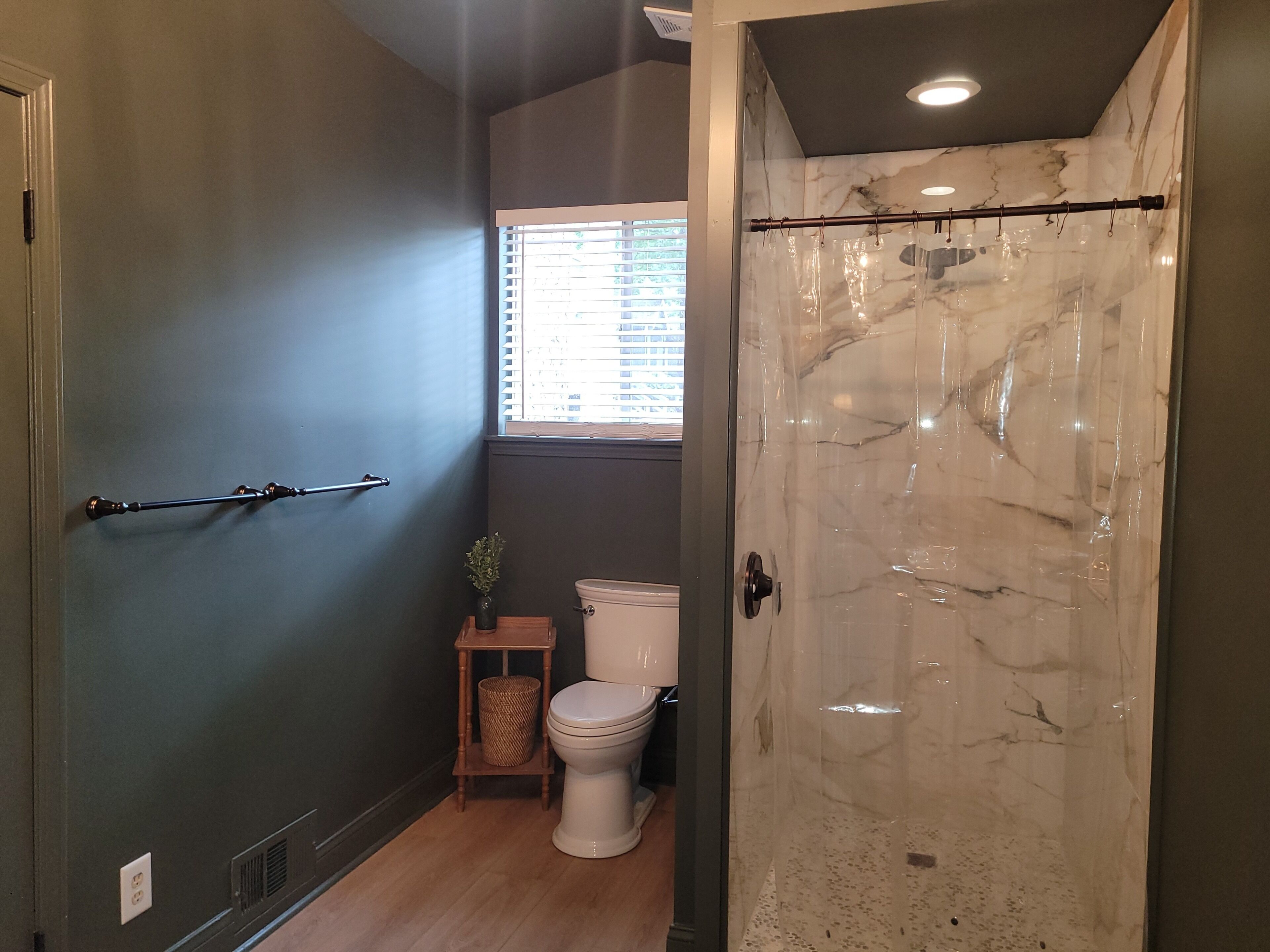 A bathroom with a shower, toilet, and a window with blinds.
