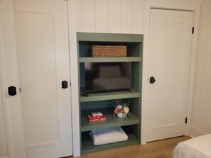 A room with a green shelving unit against a white door, containing a basket, a flat-screen TV, and some decorative items.