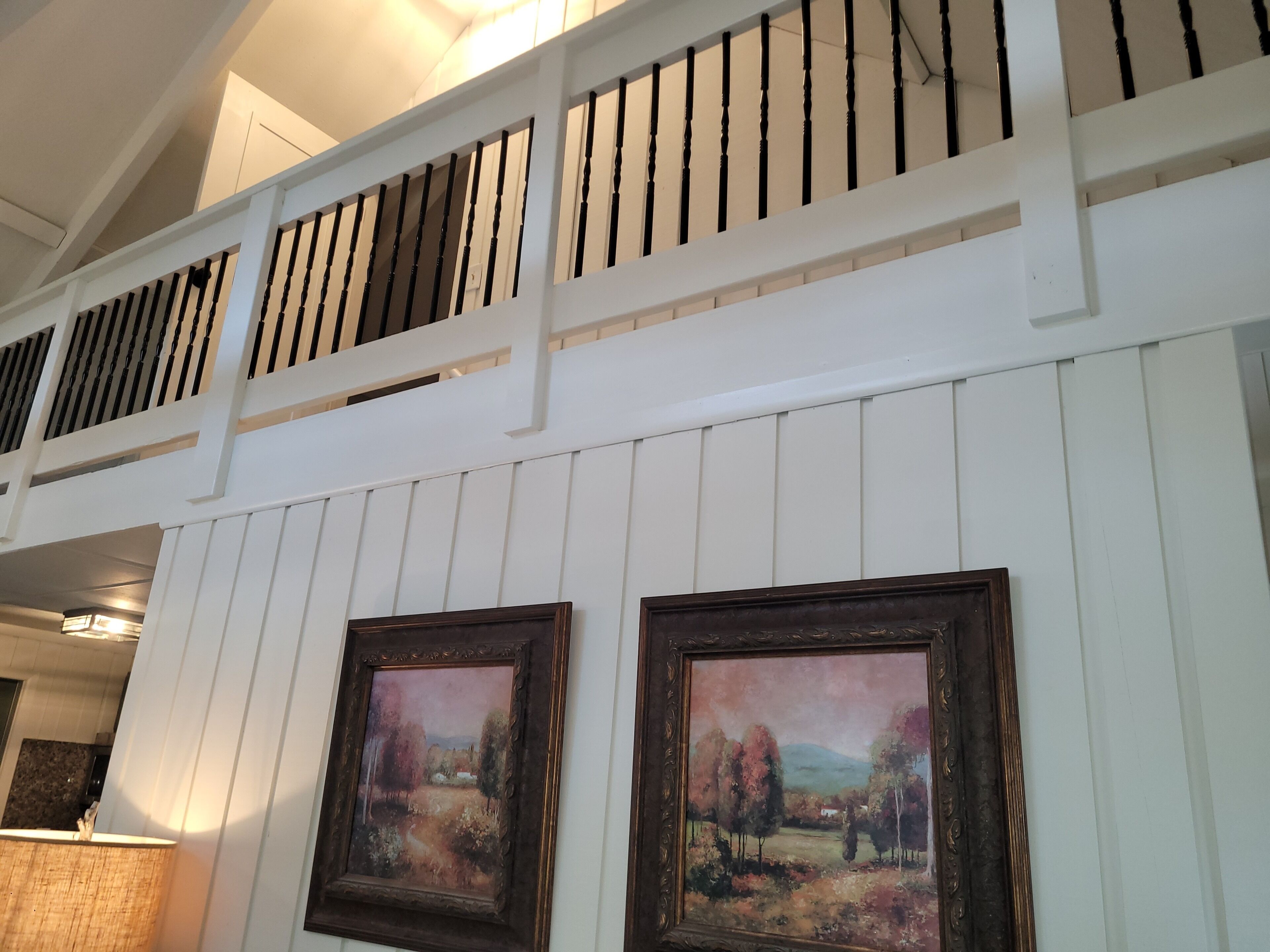 A room with white paneled walls, a wooden railing, and two framed paintings.