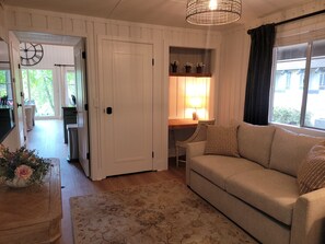 A living room with a sofa, a dining table with chairs, a kitchen area, and a door leading to an outdoor space.