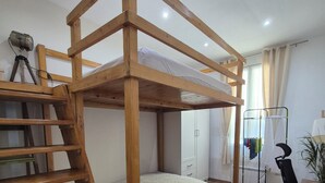 A bunk bed with a wooden ladder, a desk, and a chair in a room with a wardrobe and a plant.