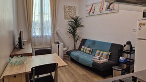 A compact living space with a dining table, a sofa, a TV, and a kitchen area.