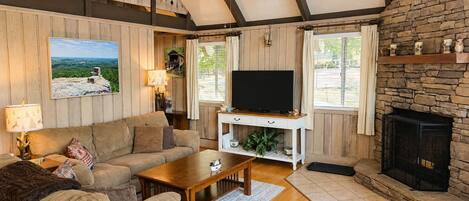 A cozy living room with a sofa, coffee table, TV, fireplace, and wooden walls.