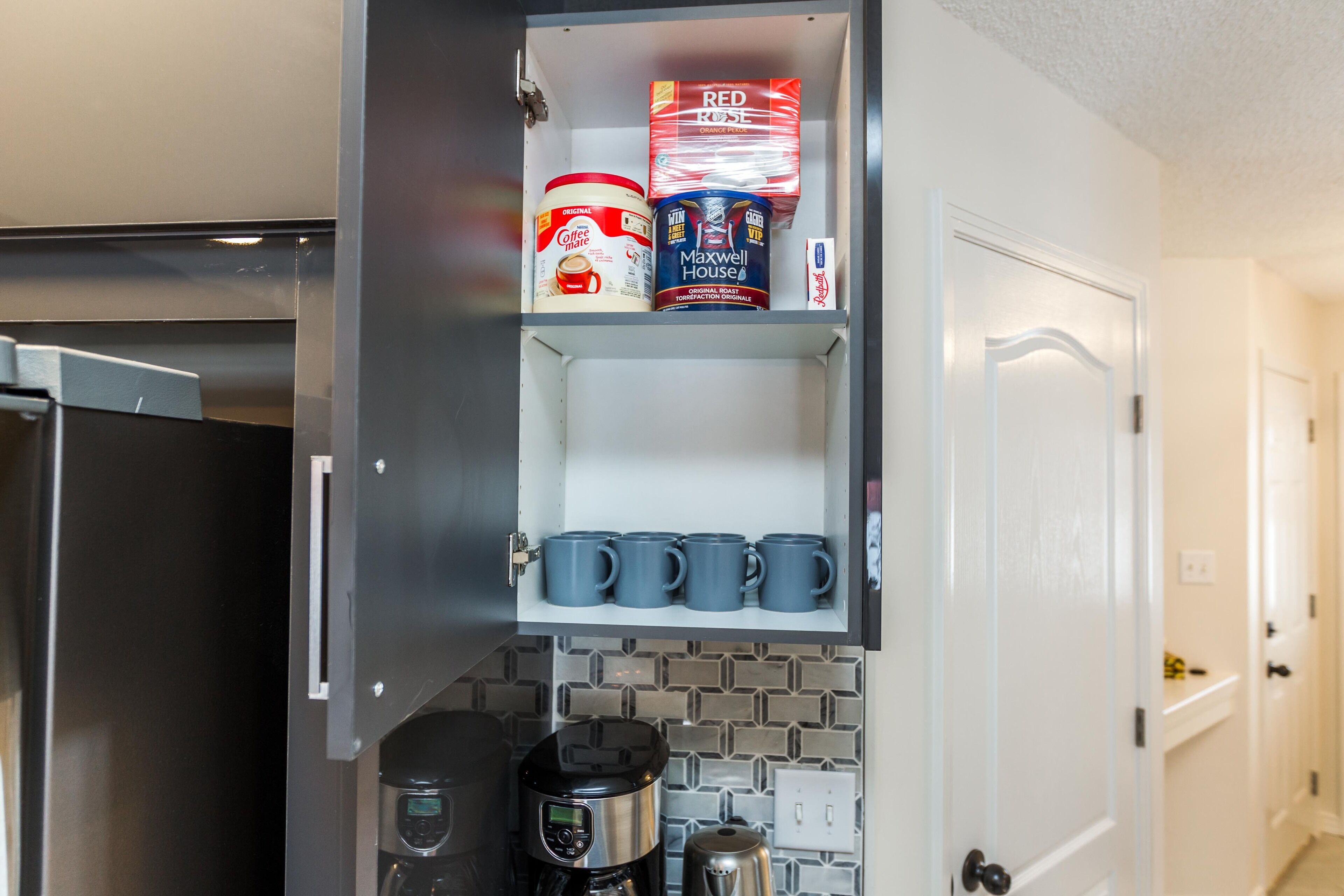 A kitchen with a coffee maker, a shelf with coffee cans, and a door.