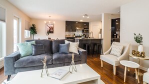 Un salon moderne avec un canapé gris, une table basse blanche et une cuisine en arrière-plan.