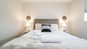 Un lit bien fait, avec du linge de lit blanc et une couverture moelleuse, deux tables de chevet avec des lampes et une tête de lit capitonnée.