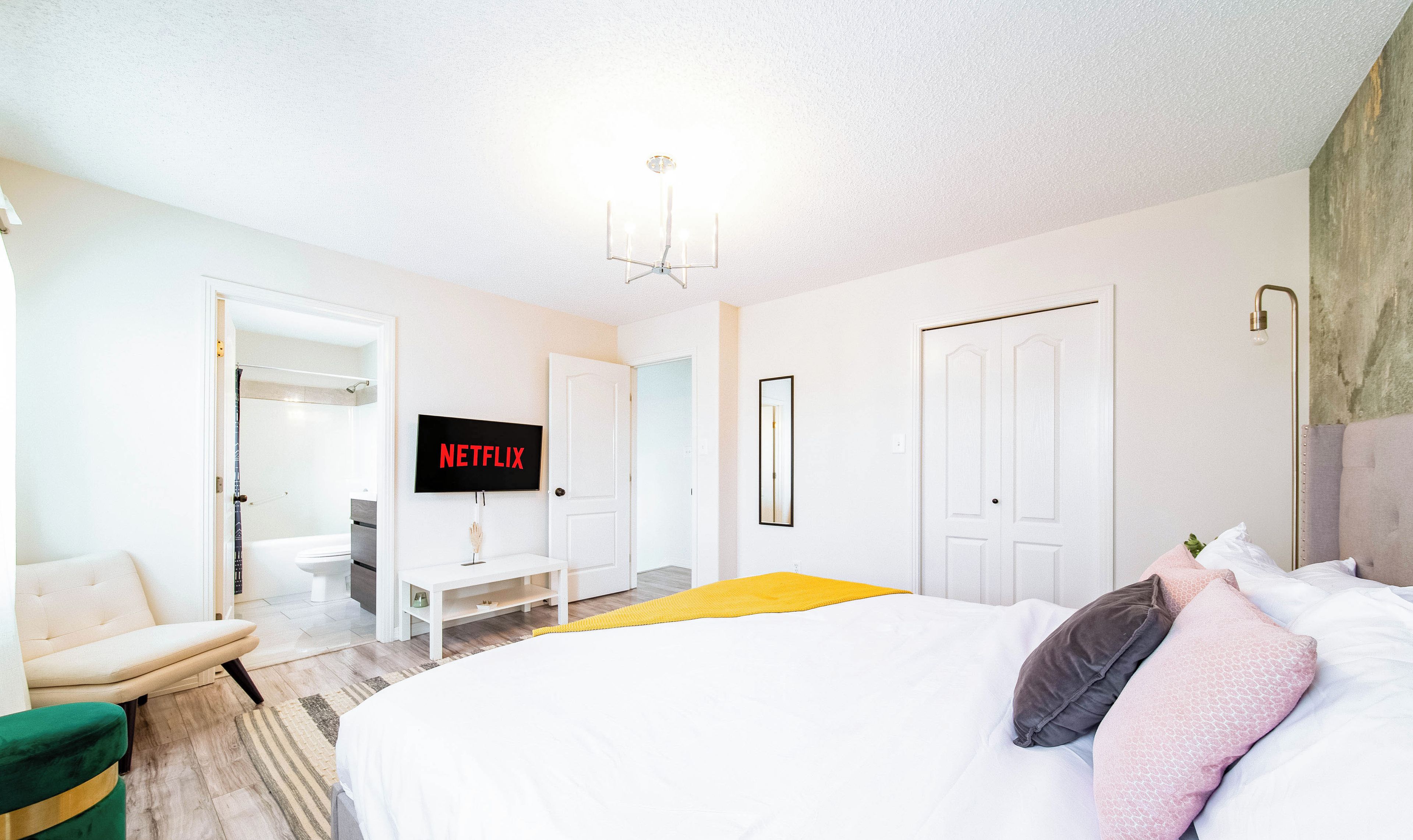 Una camera da letto moderna con un letto grande, una TV a parete, una sedia e una piccola scrivania.