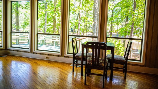 A room with large windows, wooden flooring, and a table with chairs.