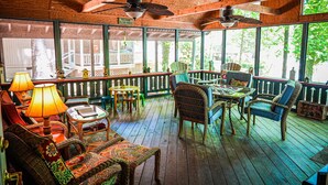Una terraza de madera con mobiliario de mimbre, ventiladores de techo y un letrero que dice 'Welcome to the Porch'.