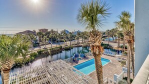 A pool area with palm trees, a clear sky, and a view of a distant building. - Cabana 30A Gulf Place Cabanas 303 (Santa Rosa Beach)