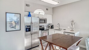 A modern kitchen with white cabinets, stainless steel appliances, a wooden dining table, and a decorative seahorse on the countertop. - Cabana 30A Gulf Place Cabanas 303 (Santa Rosa Beach)