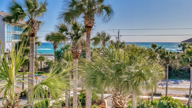 A coastal view with palm trees, a beach, and a building with large windows overlooking the ocean. - Cabana 30A Gulf Place Cabanas 303 (Santa Rosa Beach)