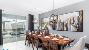 A modern dining area with a long wooden table, multiple chairs, and a large abstract painting on the wall. - Walk to Target, Private pool and SPA, StoreyLake 20037 (Kissimmee)
