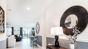 A modern living room with a dining area, a large decorative mirror, and a console table with a vase. - Walk to Target, Private pool and SPA, StoreyLake 20037 (Kissimmee)