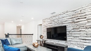 A modern living room with a stone wall, a flat-screen TV, and a sofa set. - Walk to Target, Private pool and SPA, StoreyLake 20037 (Kissimmee)
