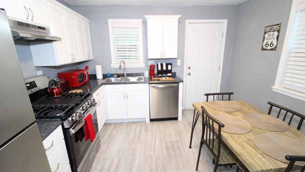 A modern kitchen with white cabinets, stainless steel appliances, and a wooden dining table with four chairs. - Recently remodeled house near Expo, TU,  Rt 66, Downtown with large fenced yard (Tulsa)