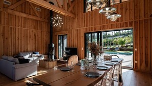 Interior de madera con zona de comedor, sofá y ventanas amplias con vistas a un jardín.