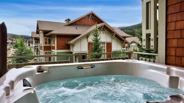 A hot tub with a wooden deck and a view of a two-story house with a sloped roof.
