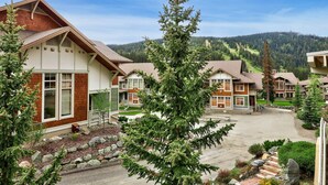 A residential area with houses featuring pitched roofs and large windows, surrounded by a mountainous landscape.