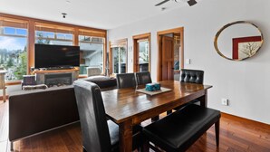 A spacious living area with a wooden dining table, black leather chairs, a flat-screen TV, and a fireplace.