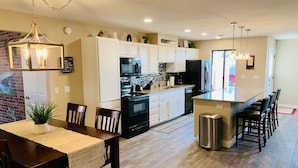 A modern kitchen with white cabinets, a central island with bar stools, and a dining area with a table and chairs. - Havasu Retreat with Pool and  Game Room-pet friendly. (Lake Havasu City)