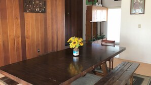 A wooden dining table with benches, a vase of sunflowers, and a wooden wall panel. - Sunshine House (Ellis)