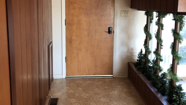 A hallway with a wooden door, a stone-patterned floor, and a planter with greenery. - Sunshine House (Ellis)