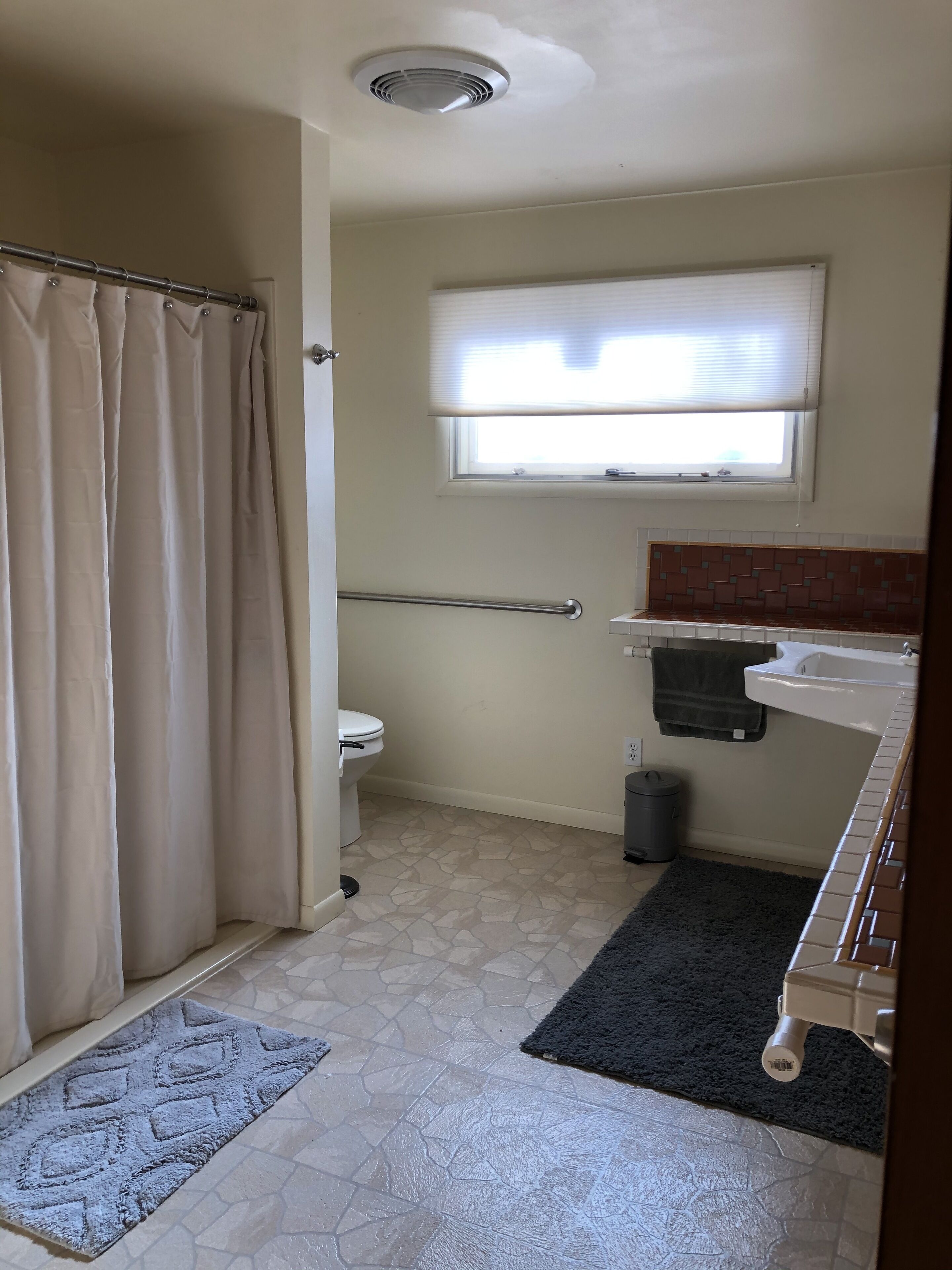 A bathroom with a toilet, a window, a shower curtain, a towel rack, and a waste bin.