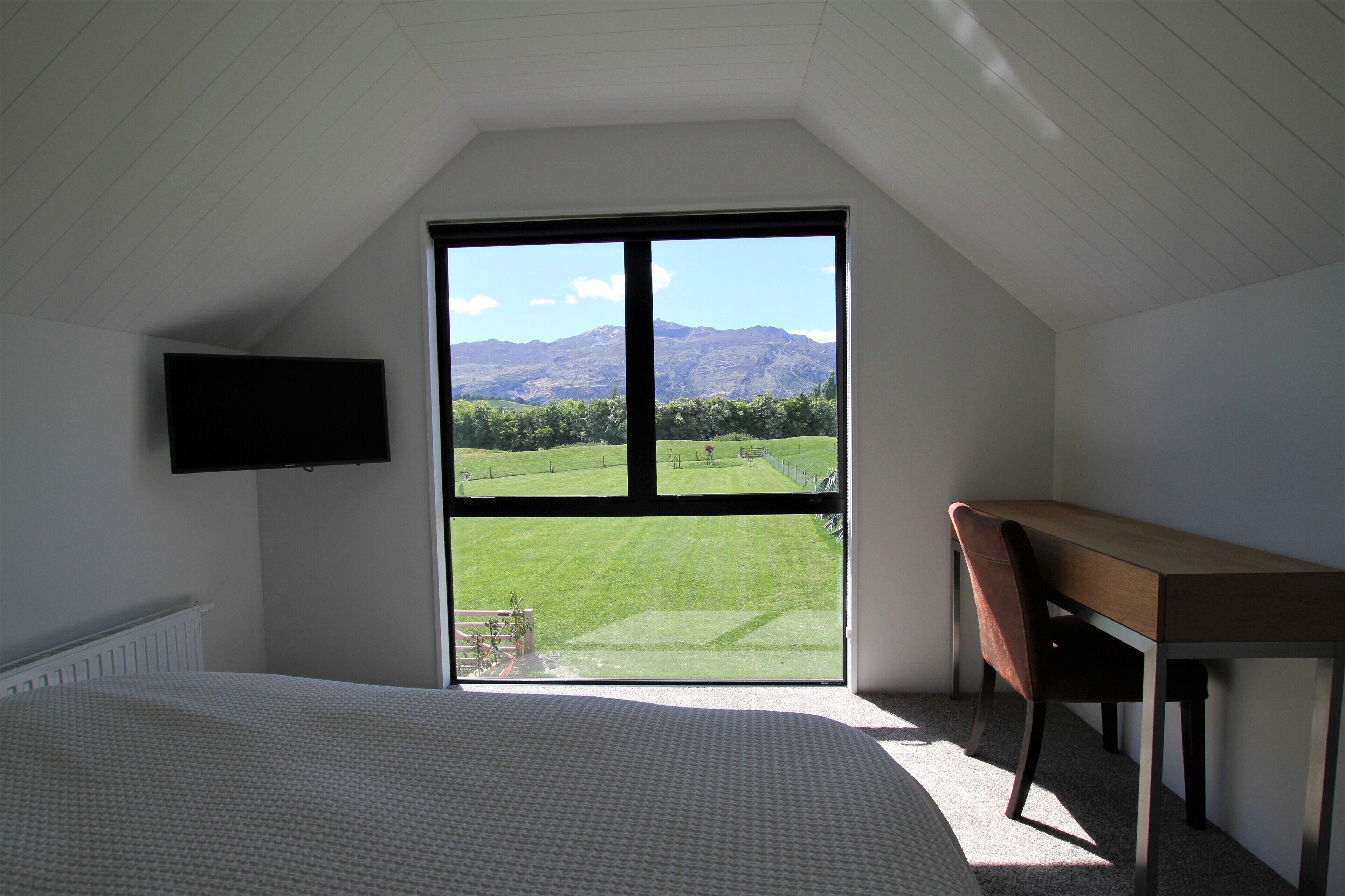 A bedroom with a large window, a bed, a desk, and a chair.