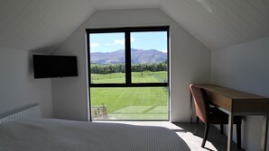 A bedroom with a large window, a bed, a desk, and a chair.