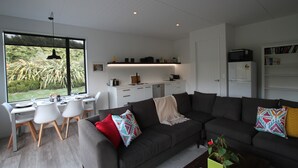 A modern living room with a dark grey sofa, a dining area with white chairs, and a kitchen with white cabinets.