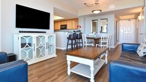 A living room with a TV, blue leather sofa, and a dining area with a table and chairs. - Updated 2 Bedroom Condo on the 6th Floor at The Palms of Destin - 2616 (Destin)