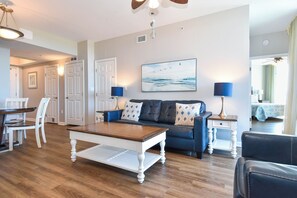 Uma sala de estar com uma mesa de centro de madeira, um sofá azul com almofadas estampadas e um quadro com pássaros na parede.