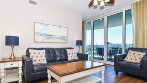A modern living room with a leather sofa, a wooden coffee table, and a large window offering a city view. - Updated 2 Bedroom Condo on the 6th Floor at The Palms of Destin - 2616 (Destin)