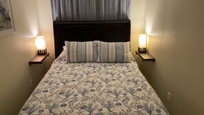 Una cama con una colcha estampada, dos lámparas de noche y un cabecero.