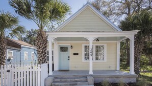 A two-story house with a porch, a white picket fence, and palm trees.
