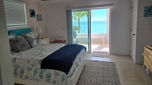 Un dormitorio con cama, ventilador de techo, ventana con persianas y vista al océano.
