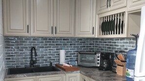 Una cocina con armarios de colores claros, un lavamanos negro, un microondas y una cafetera.