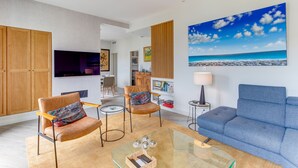 A modern living room with leather armchairs, a glass coffee table, and a large painting of a beach. - LA TERRASSE DU PORT AP4212 (Niza)