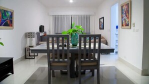 Un espace de repas moderne avec une table et des chaises en bois, un vase avec une plante et un canapé en arrière-plan.