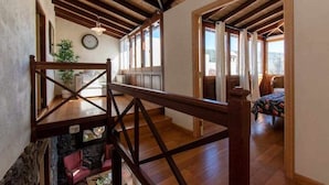 A spacious room with wooden beams on the ceiling, a bed with a floral bedspread, and a view of the outdoors through large windows.