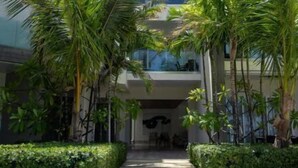 Un immeuble moderne à plusieurs étages, doté de balcons, entouré d’un espace vert bien entretenu et bordé d’un chemin dégagé.