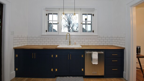A kitchen with a wooden countertop, dark cabinets, a stainless steel dishwasher, and a window with a view of bare trees. - Vintage Gem in the Heart of Sheridan (Sheridan)