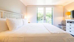 Et hotelværelse med en stor seng, et kommode, et fjernsyn og en balkon med udsigt over grønne områder.