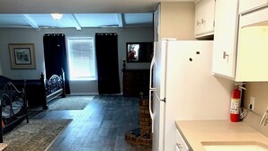 Un'ampia cucina con una grande isola, un frigorifero e un lavello. C'è un'area pranzo con tavolo e sedie, e una camera da letto con un letto e una finestra.
