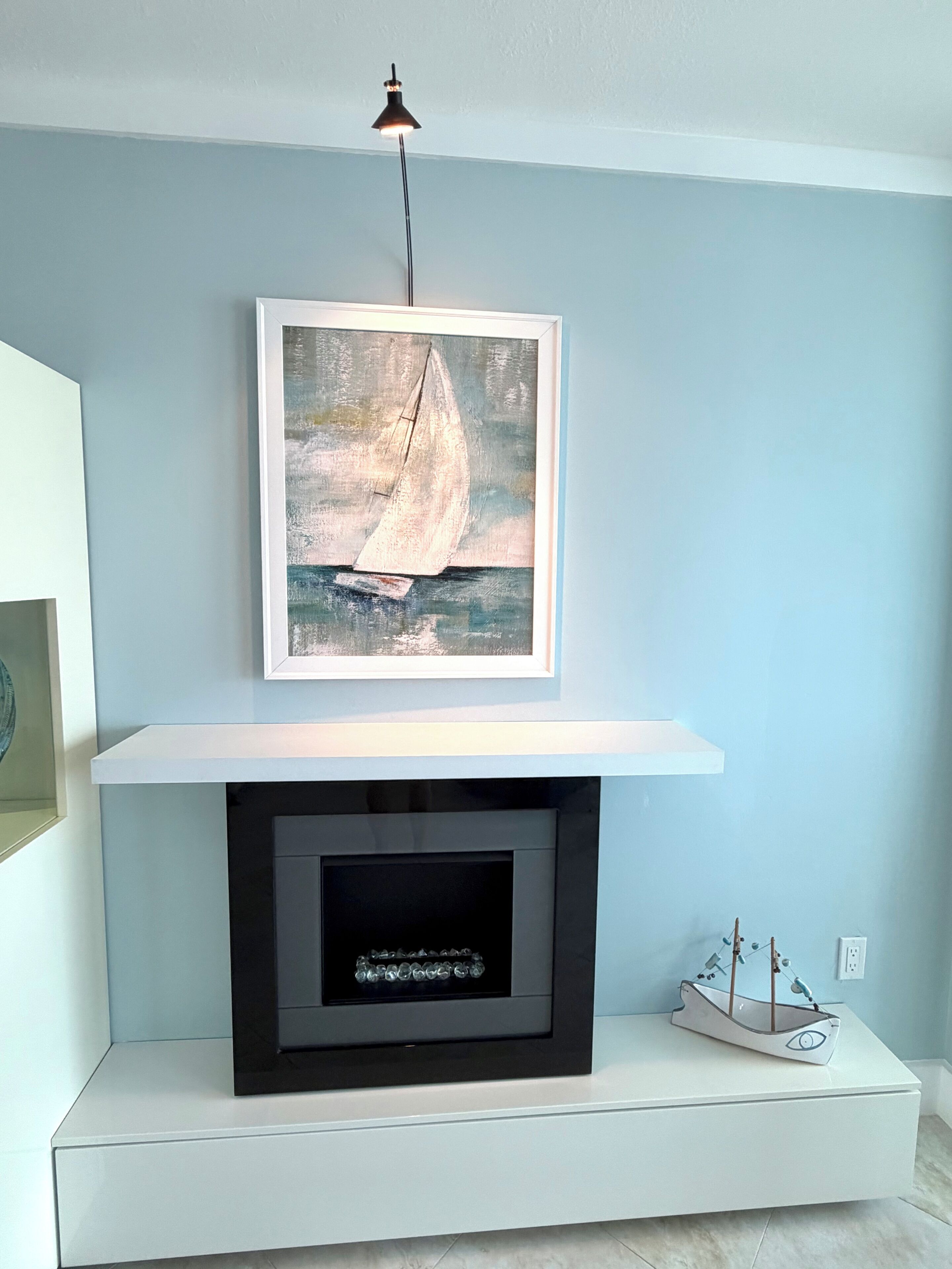 A room with a white fireplace, a framed painting of a sailboat, and a small ship model on the mantel.