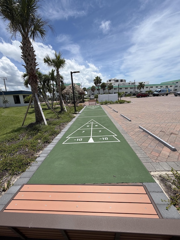 A green pathway with a hopscotch game, palm trees, and a parking area with a building in the background.
