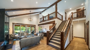 A spacious living area with a large gray sofa, wooden flooring, and a staircase with wooden railings leading to an upper level. - Beautiful Suncadia House With Two Master Bedrooms and plenty of space for kids!  (Cle Elum)