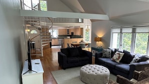 Un vaste espace de vie doté d’un haut plafond, d’un escalier menant à un niveau supérieur, d’une cuisine et d’un coin salon avec une grande fenêtre.